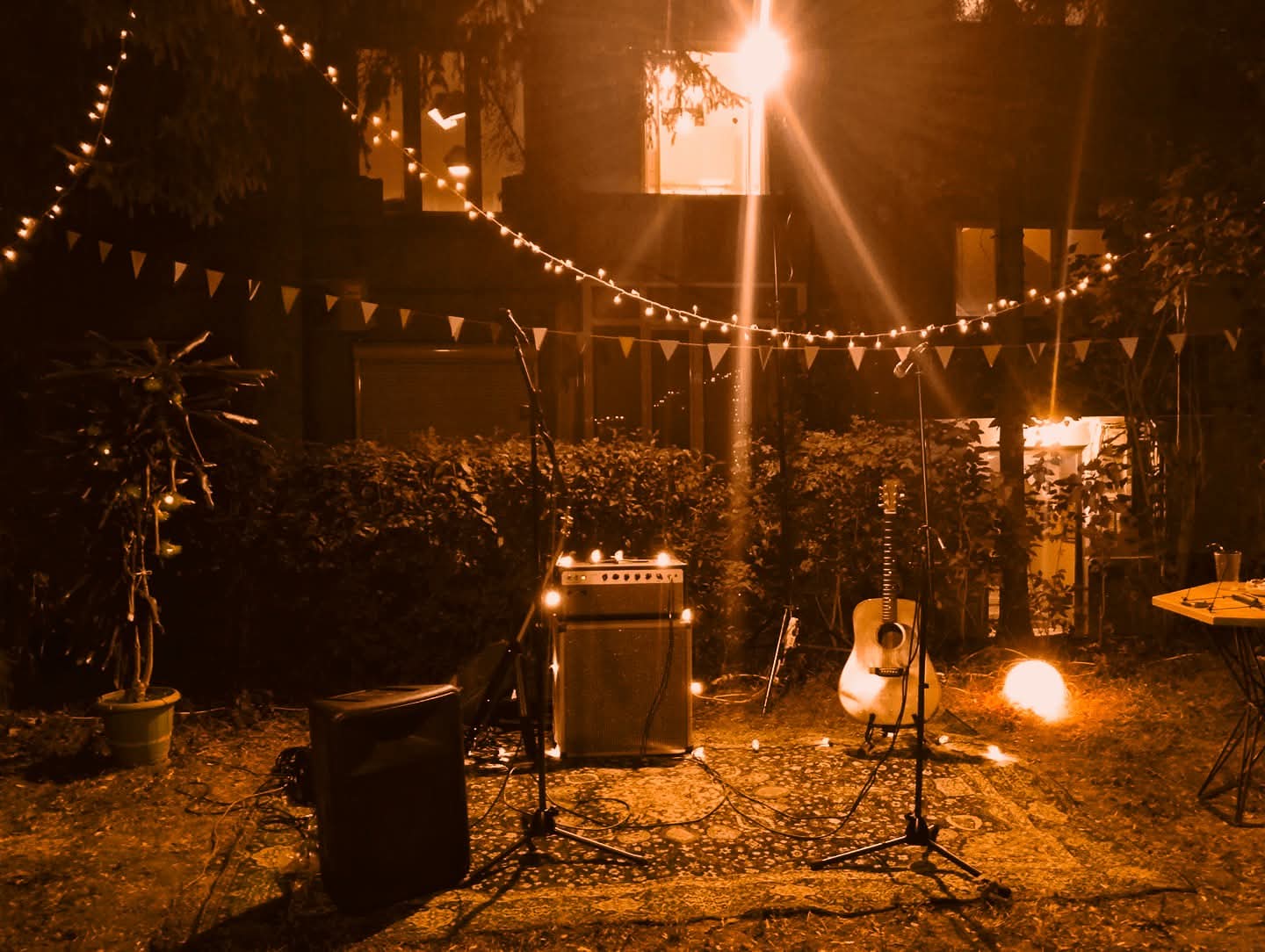 An intimate outdoor performance setting with guitars, microphones, and warm string lights